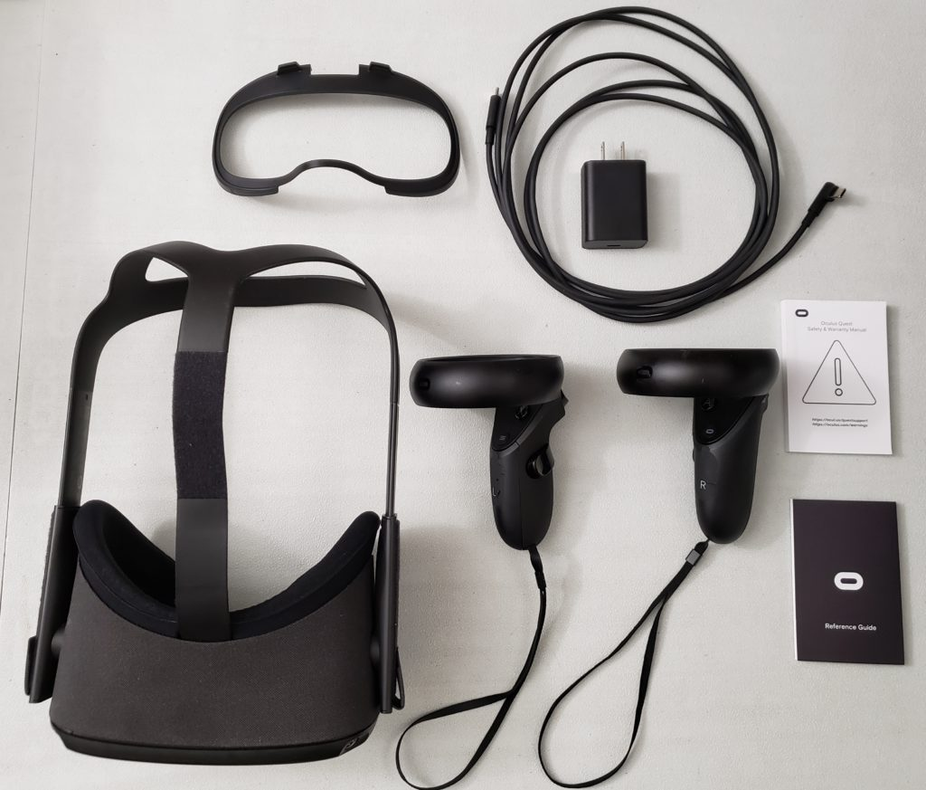 All contents of an oculus quest 1 box laid out on a table. Clockwise from top: Charging cable, Power Adapter, Regulatory manual, Controllers, Reference Guide, HMD, Glasses spacer