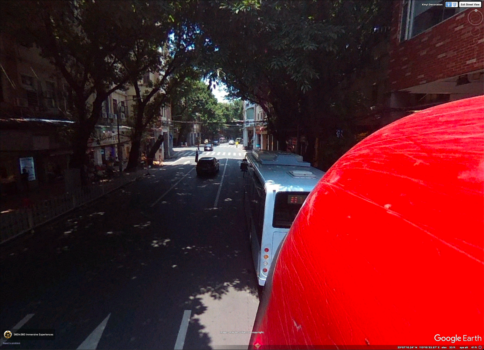 Google Earth photosphere screenshot, showing shaded road in china. Camera is next to bright red bus, white bus visible ahead of it in traffic. one way street.