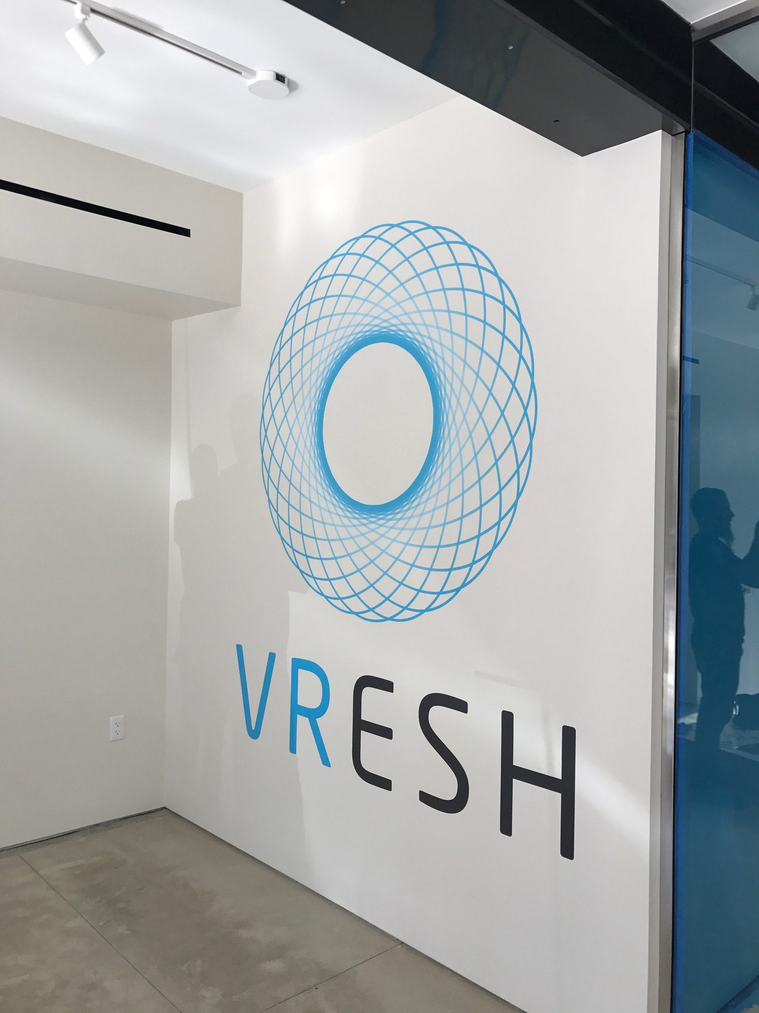 photo of wall inside building, with spirograph logo and "VRESH" text below