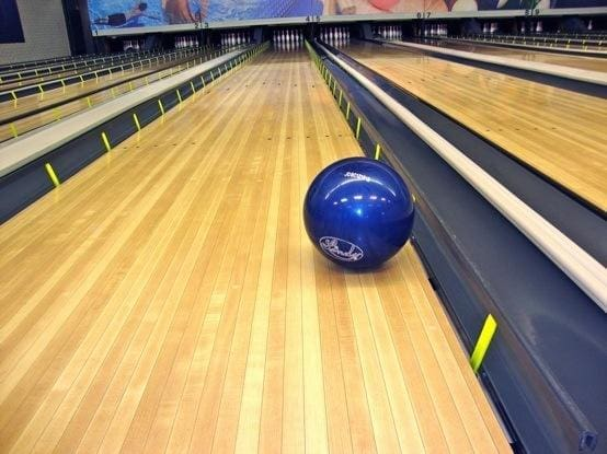 blue bowling ball resting on a bowling lane, leaning against a black gutter bumper with yellow supports.